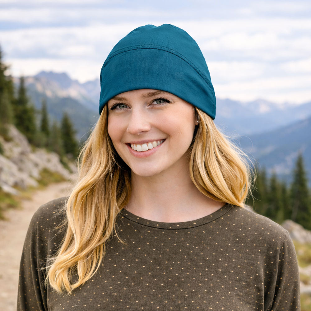 woman wearing the eclipse beanie in spirulina with the mountains in the background and she is also wearing the eclipse equinox cover-up