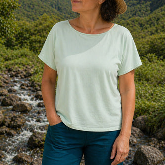Woman standing in a natural setting with mountains and a stream in aqua boatneck