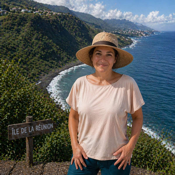 Woman standing in front of a scenic view with ocean and mountains, wearing a hat and a light-colored eclipse Boatneck shirt.