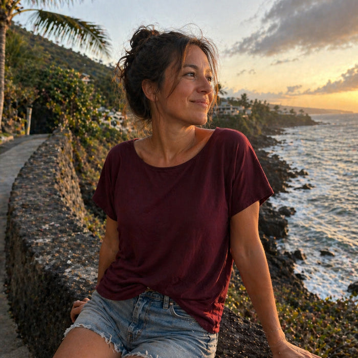 Woman sitting by the ocean at sunset with palm trees in the background wearing the eclipse Boatneck 