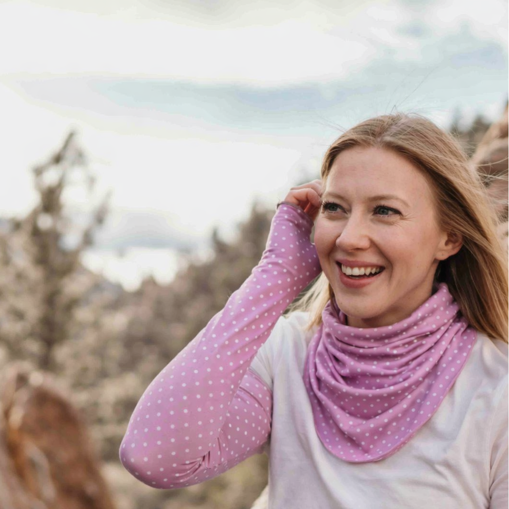 Woman wearing a pink polka dot eclipse Gaiter and Sun Sleeves outdoors with rock formations in the background