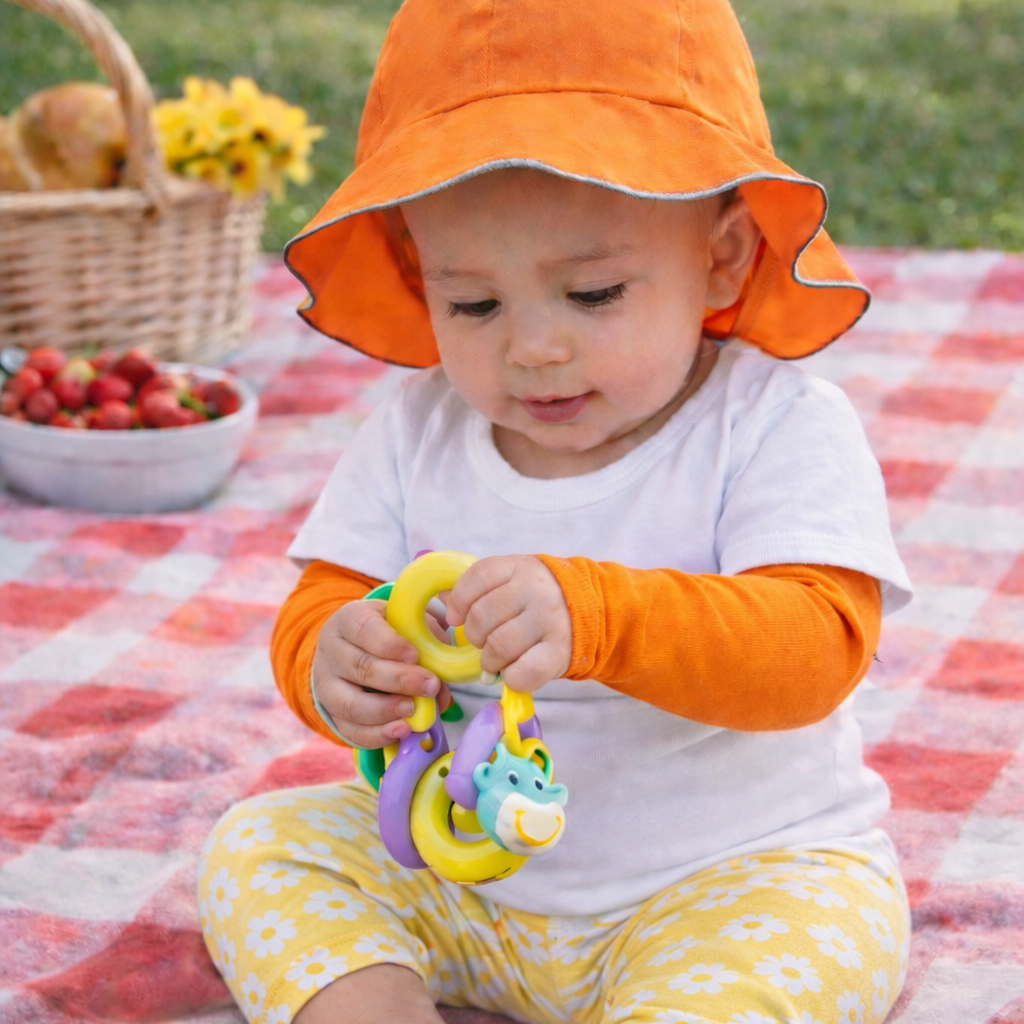 baby sitting on picnic blanket playing with toy wearing eclipse sun sleeves for children in orange in upf50