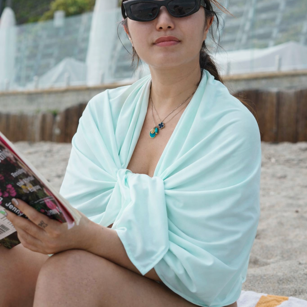 Woman sitting on a beach reading a book, wearing sunglasses and the eclipse Wrap.
